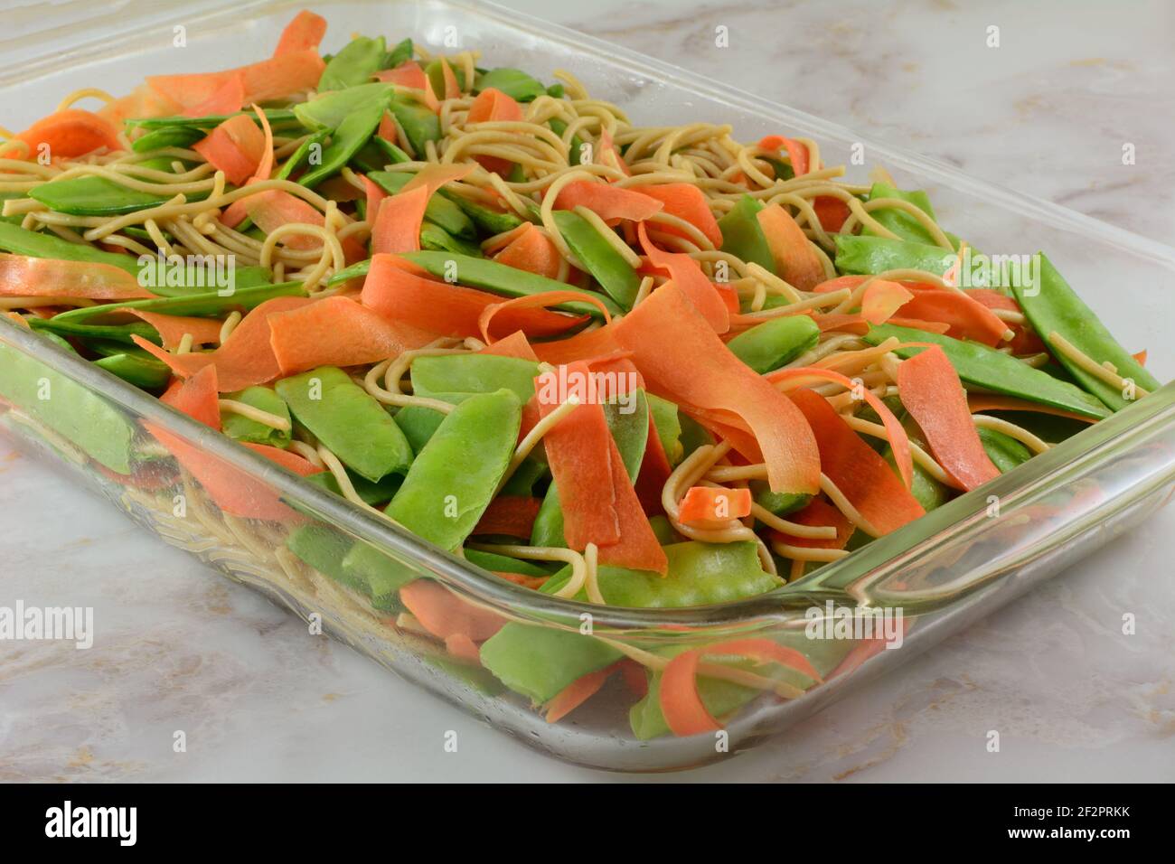 Piselli di neve e carote crudi e casseruola di pasta cotta strati per la cottura in teglia di vetro Foto Stock