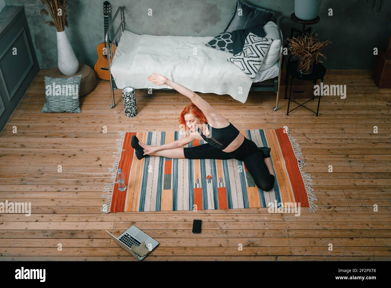 Una ragazza fitness sportiva forte e bella in swears sportivi che si allunga nella sua camera da letto luminosa e ariosa con un interno minimalista. Foto Stock