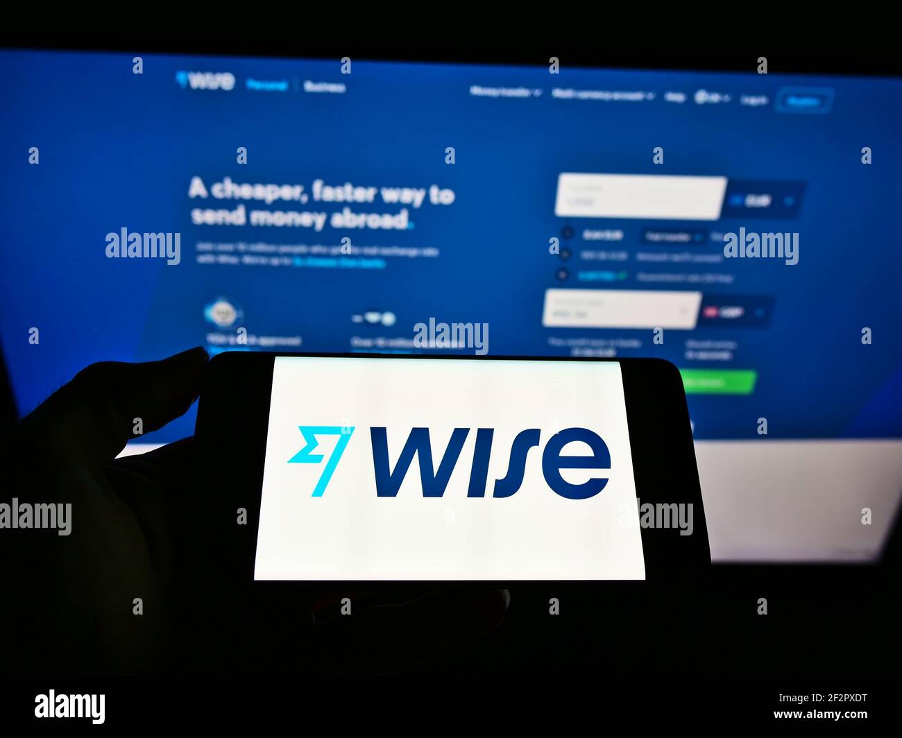 Persona che tiene il cellulare con il logo della società di pagamento elettronica Wise (TransferWise Ltd.) sullo schermo di fronte alla pagina web. Mettere a fuoco il display del telefono. Foto Stock
