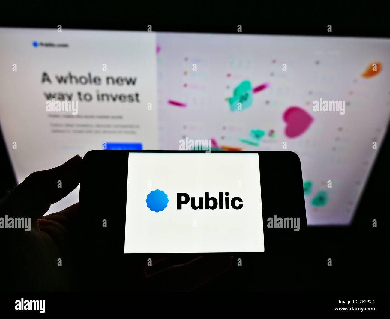 Persona che tiene il cellulare con il logo della piattaforma di investimento Public.com (Public Holdings Inc.) sullo schermo davanti alla pagina web. Mettere a fuoco il display del telefono. Foto Stock