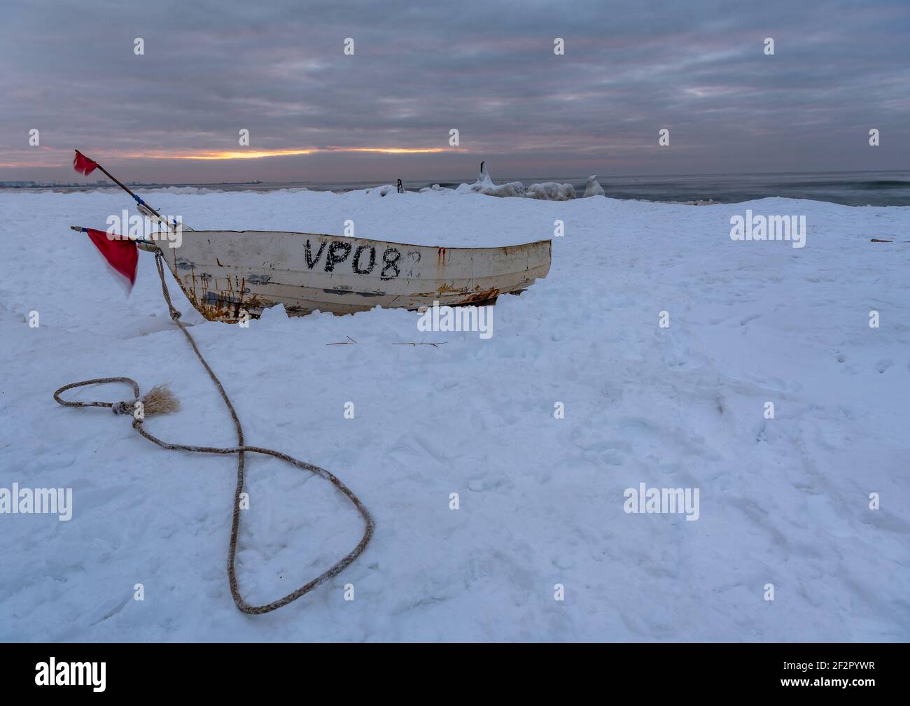 una barca bianca è tirata fuori sulla riva del mare in inverno e la riva del mare è coperta di neve ma c'è ghiaccio sotto di esso e c'è un tramonto sul ho Foto Stock