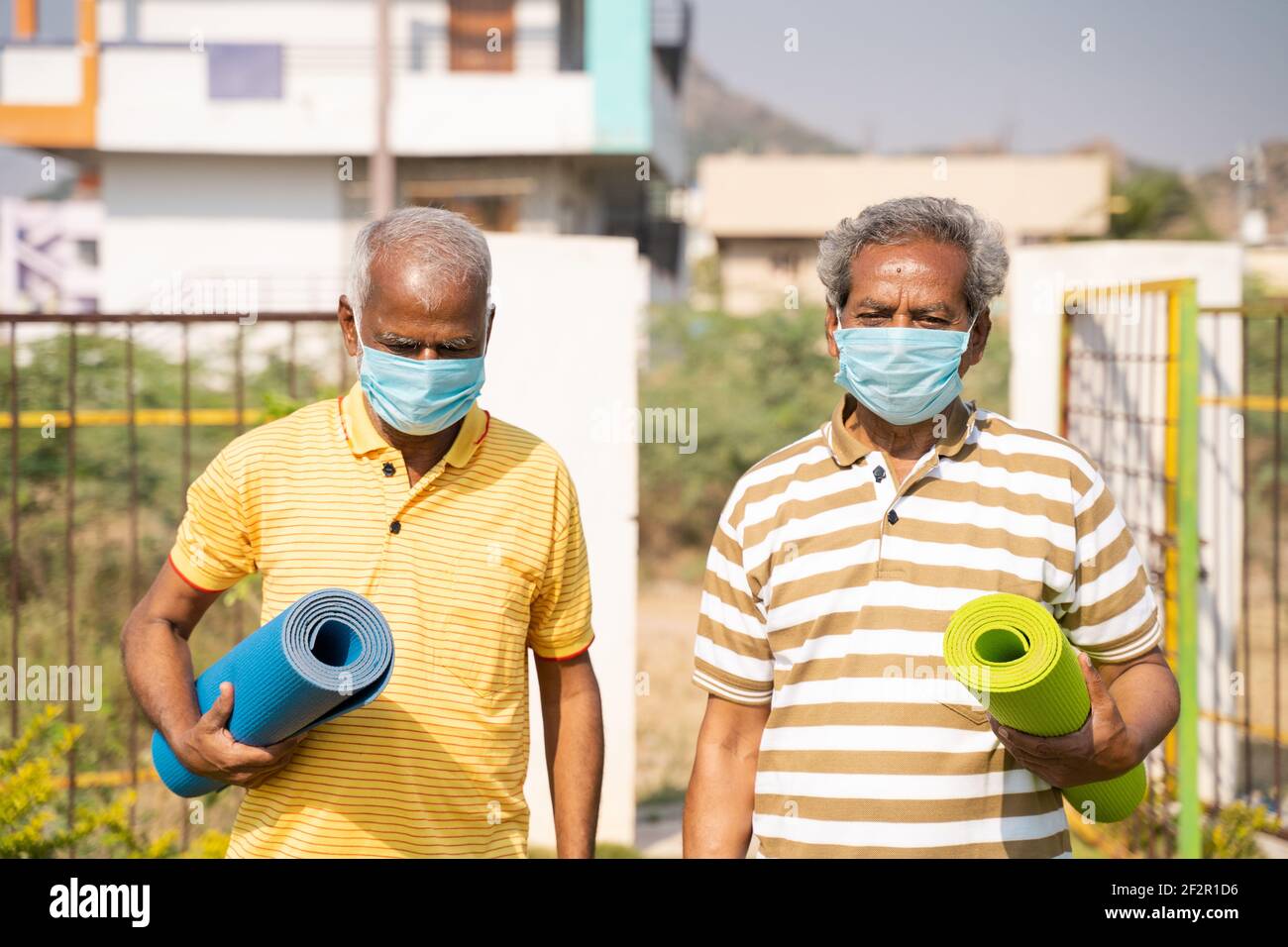 Due persone anziane con tappetino yoga e maschera medica Nel parco - uomini anziani sani con tappetino fitness in arrivo per lo yoga durante il coronavirus covid-19 Foto Stock