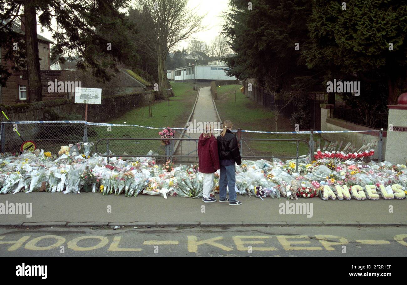 File foto datata 14/03/96 di bambini che si fermano a guardare i fiori lasciati alla Dunblane Primary School, dove sedici bambini e insegnante Gwen Mayor sono stati assassinati dal gunman Thomas Hamilton quando ha aperto il fuoco su una classe palestra il 13 1996 marzo. Data di emissione: Sabato 13 marzo 2021. Foto Stock