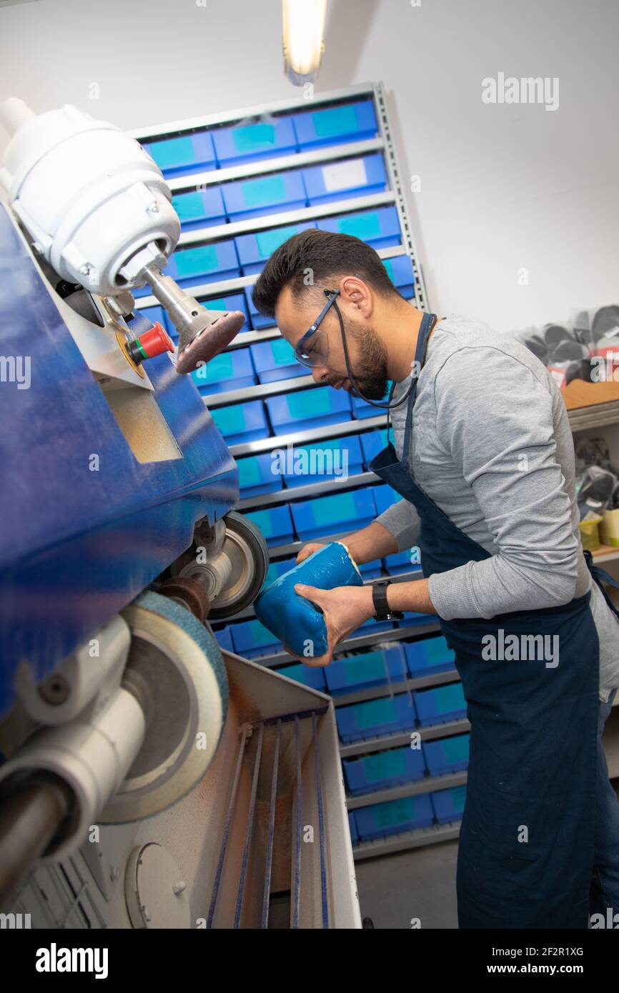 Operaio professionale che utilizza una macchina di smerigliatura presso un calzolaio. Lavoro dei dipendenti altamente concentrato.sulla creazione di una scarpa personalizzata. Foto Stock