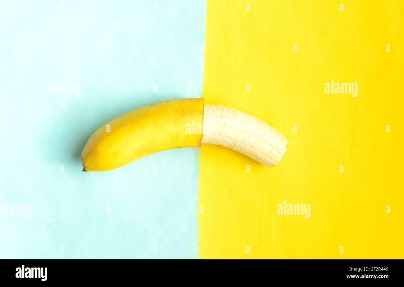 Banana parzialmente sbucciata su sfondo blu giallo.Tropic frutta estiva. Foto Stock