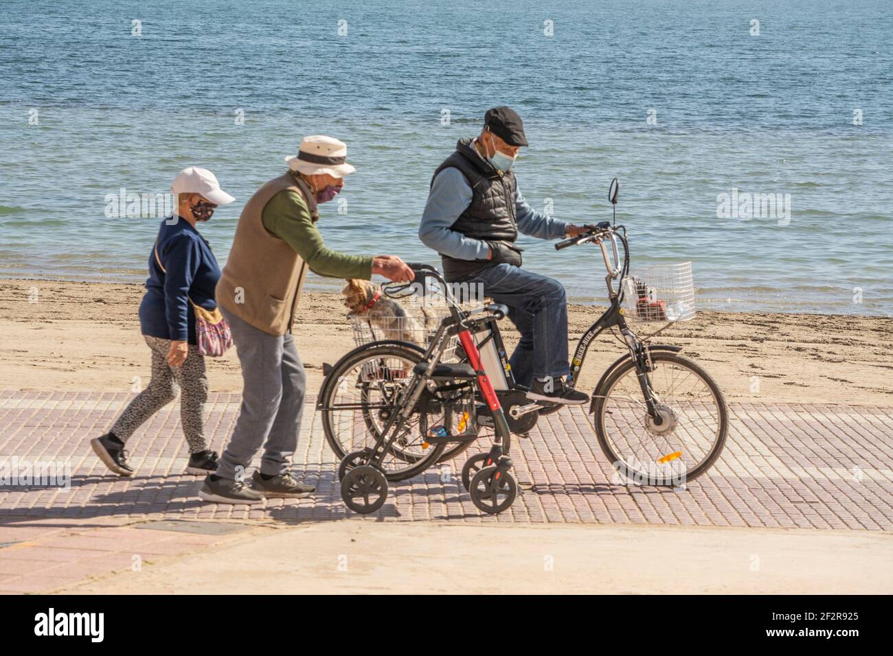 I cittadini anziani che si ordono maschere di faccia camminano e ciclano sul Promenarde dal Mar Menor a Los alcazares in Murcia Spagna Foto Stock