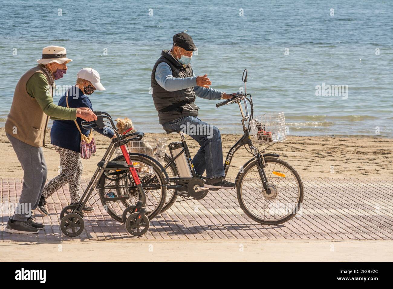 I cittadini anziani che si ordono maschere di faccia camminano e ciclano sul Promenarde dal Mar Menor a Los alcazares in Murcia Spagna Foto Stock