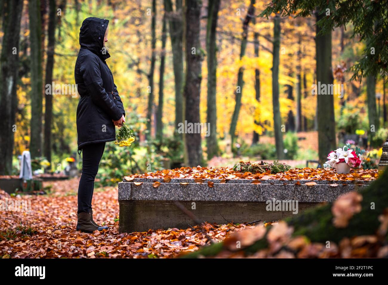 La donna triste sta piangendo per la persona morta nella tomba nel cimitero. Solitario Mourner nel cimitero d'autunno. Dolore e grido per i morti Foto Stock