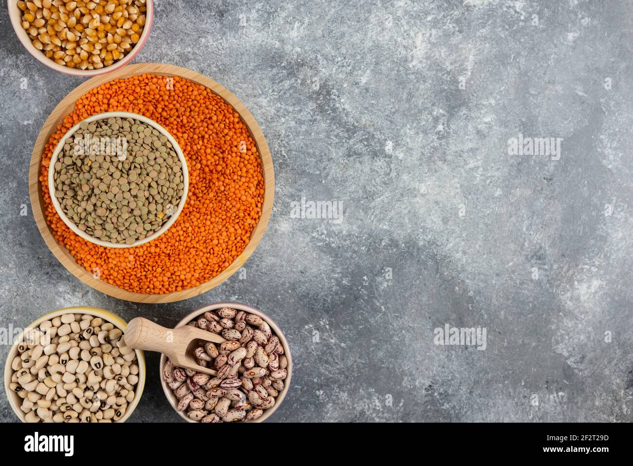Ciotole di vari fagioli, lenticchie e granelli non cotti sulla superficie del marmo Foto Stock