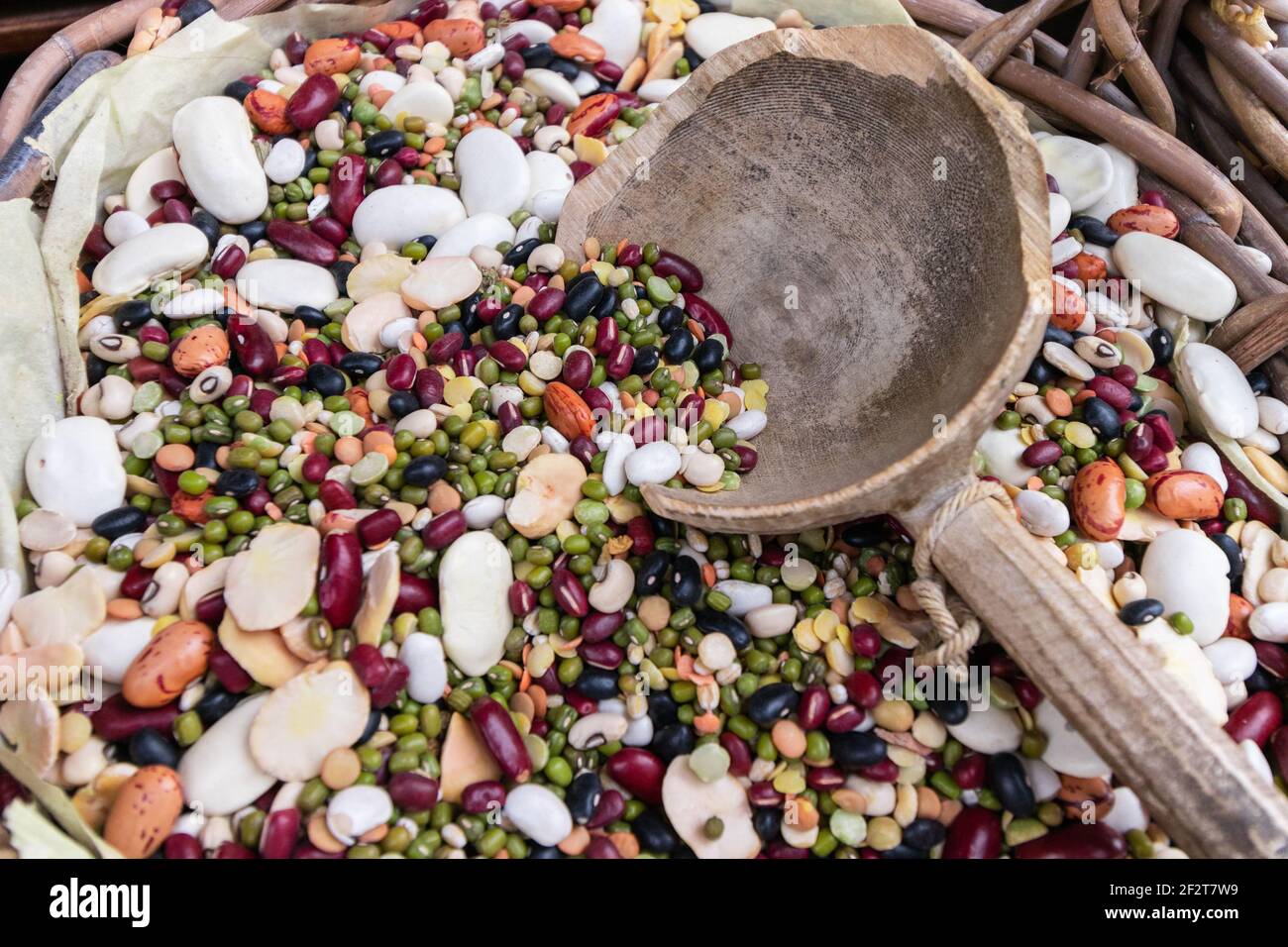 Composizione di diversi tipi di legumi. Ceci, lenticchie rosse, piselli gialli e diversi tipi di fagioli in un cesto di legno con un grande mea di legno Foto Stock
