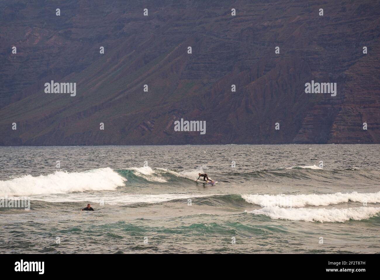 Surfisti surfing nel surf spot vicino alla spiaggia di Famara sull'isola di Lanzarote. Risco de Famara sullo sfondo Foto Stock