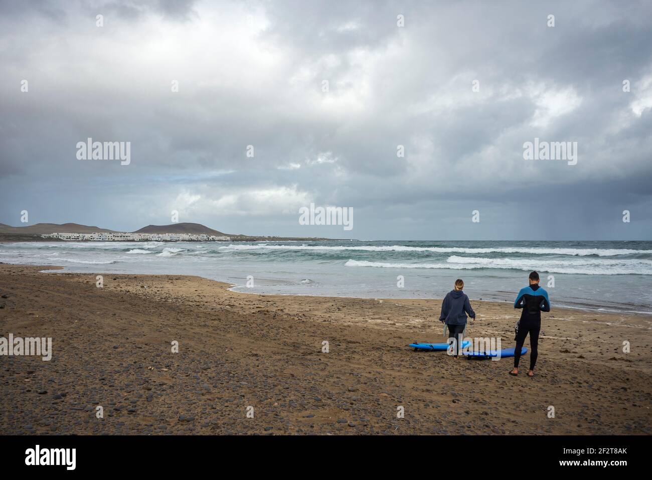 Due surfisti si preparano a fare surf nell'oceano sulla spiaggia di Famara, l'isola di Lanzarote. Stagione invernale, grandi onde nell'oceano Foto Stock