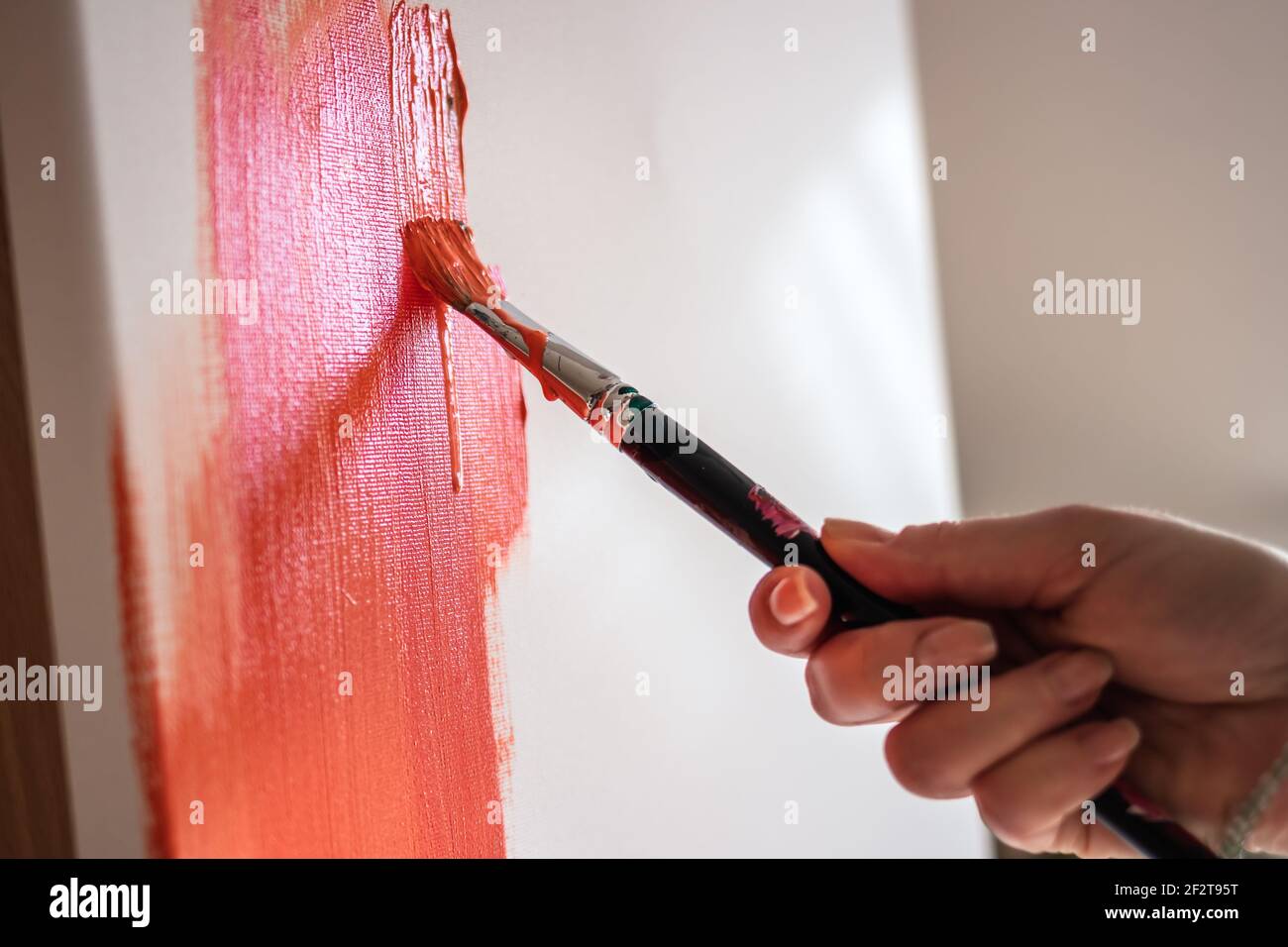 Pittura acrilica. Primo piano mano femminile con vernice a pennello su tela. Lavorare in studio d'arte Foto Stock