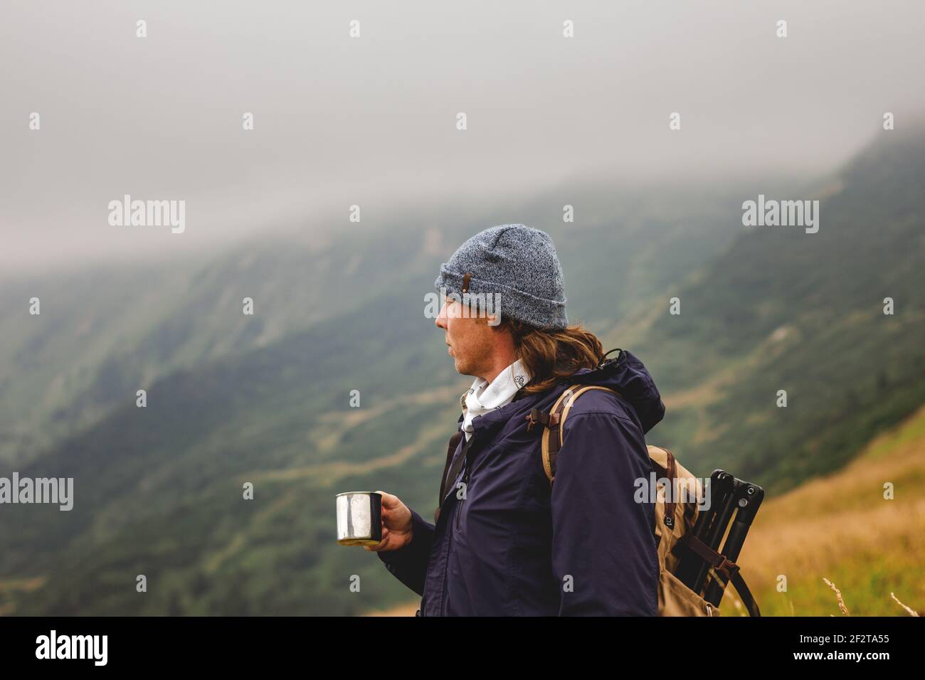 Escursionista che tiene la tazza con bevanda calda in montagna a maltempo. Concetto di viaggio, avventura e stile di vita attivo Foto Stock