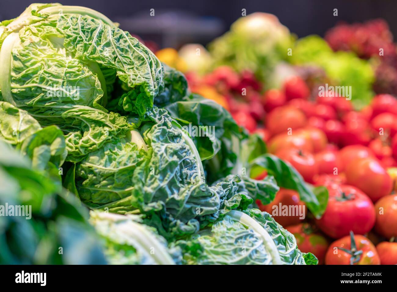 Cavoli di Savoia verdi increspati riempiono una vetrina del mercato accanto a pomodori rossi, fotografati con messa a fuoco selettiva a Barcellona, Spagna. Foto Stock
