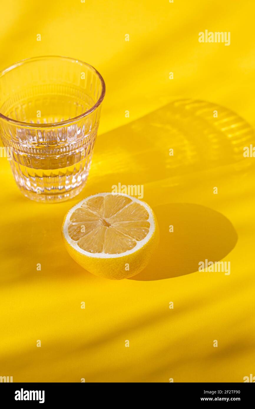 Classe di cristalli bianchi con limone su una superficie bianca o gialla, per una vita sana e olistica Foto Stock