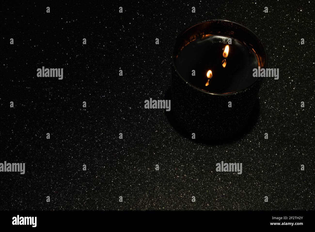 Candela nera illuminata con due pulcini su sfondo nero con scintille Foto Stock