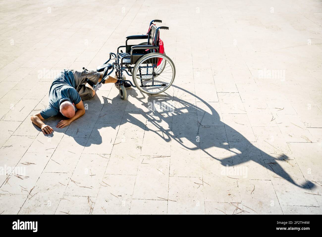 Uomo disabile con handicap che ha subito un incidente con sedia a rotelle - concetto di disabilità con una persona impotente non aiutata che giace sul pavimento Foto Stock