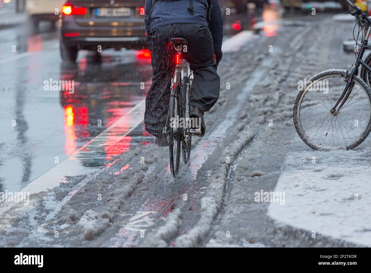 ciclista con pantaloni da pioggia su una pista ciclabile con neve slush Foto Stock