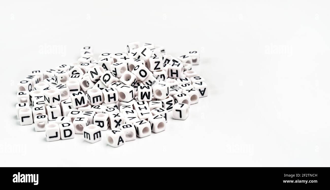 Mucchio di piccole perle cubiche bianche con varie lettere sparse sulla tavola, spazio per il testo sul lato destro Foto Stock