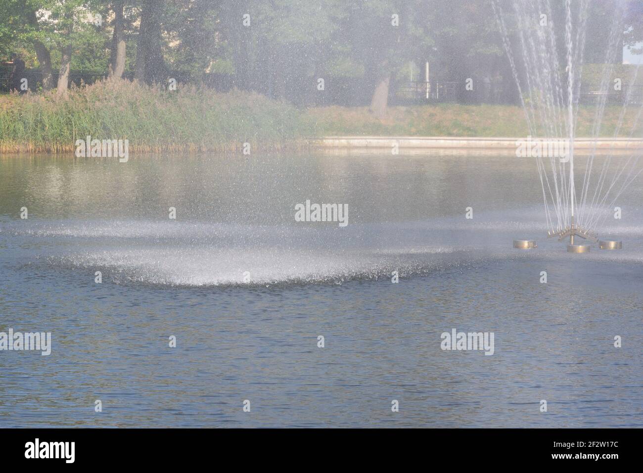Spruzzi e gocce sull'acqua del lago dalla fontana. Vista nebbia, messa a fuoco selettiva. Foto Stock