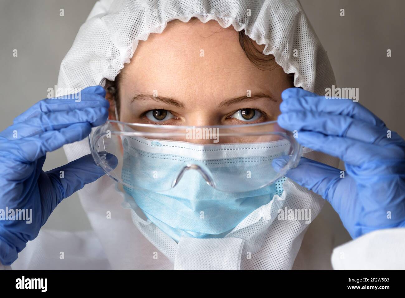 Medico femminile in primo piano tuta PPE, l'infermiere indossa occhiali medici durante la pandemia COVID-19, ritratto di medico donna che indossa maschera protettiva a causa di Foto Stock