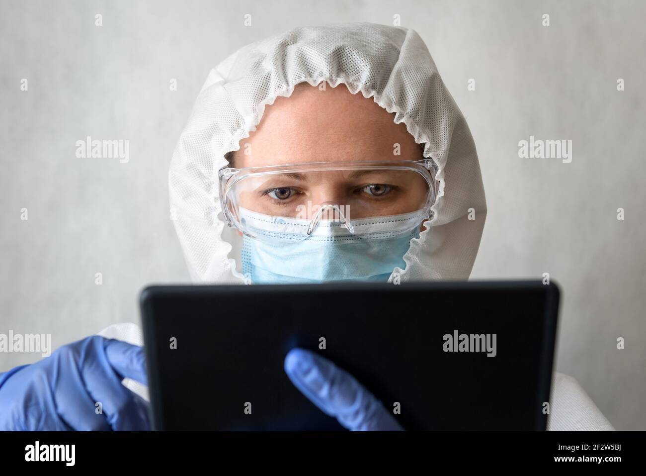 Dottore in tuta medica DPI usa tablet digitale, ritratto di infermiere femminile in occhiali protettivi e maschera durante COVID-19 coronavirus pandemia, fisica Foto Stock