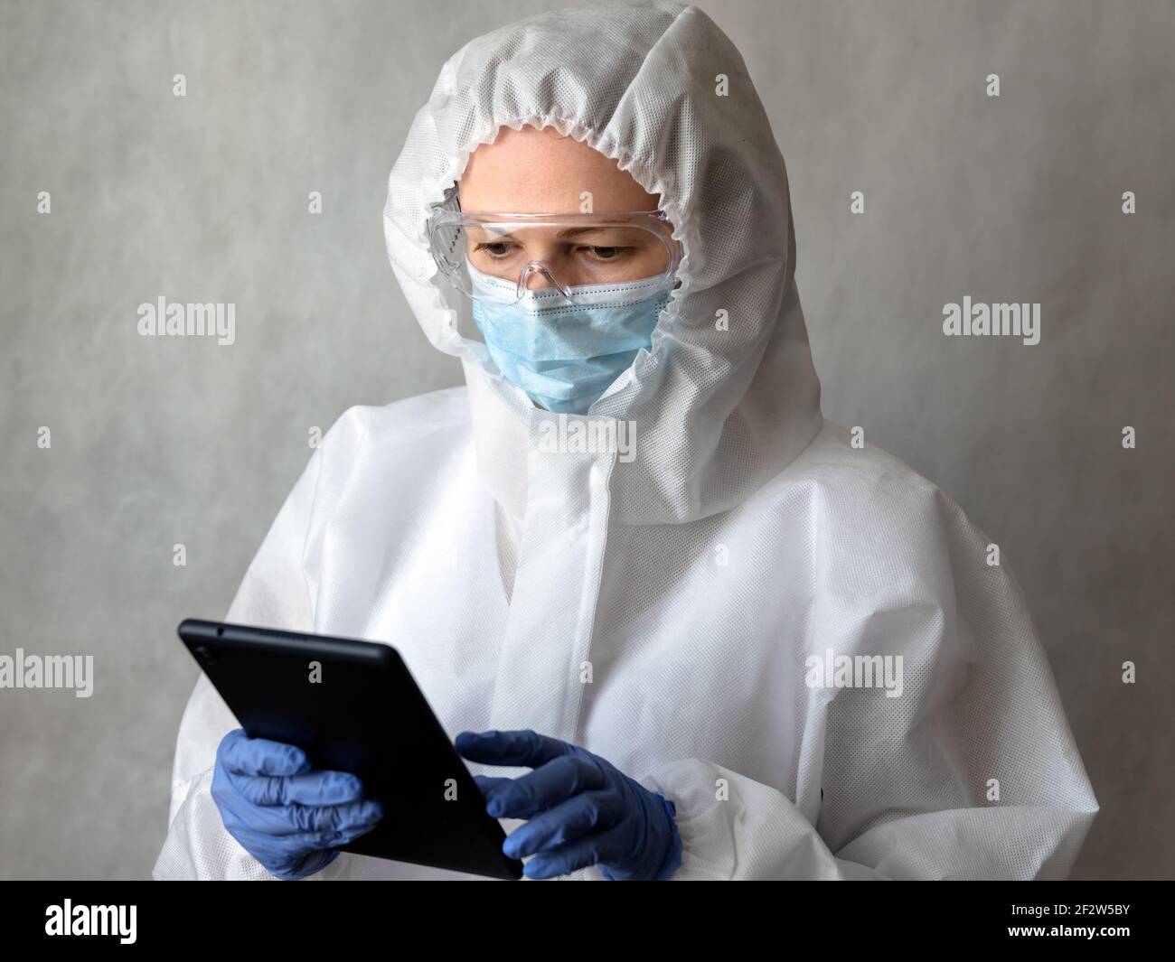 Dottore in tuta medica DPI usa compresse digitali, infermiere femmina in occhiali protettivi e maschera durante la pandemia di coronavirus COVID-19, il medico lavora con Foto Stock