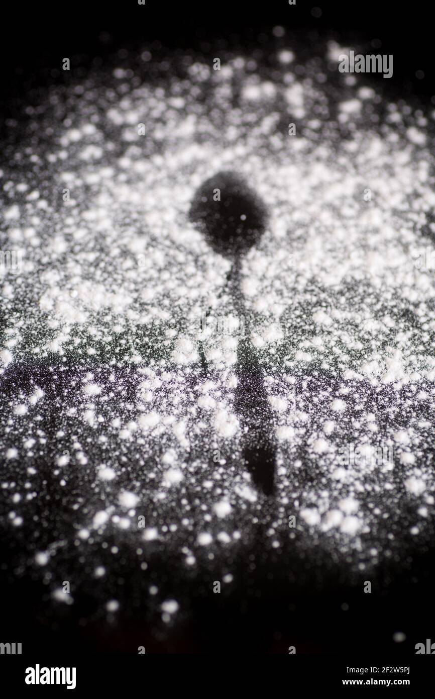 lo zucchero a velo bianco dolce e il cucchiaio si tracciano su sfondo nero Foto Stock