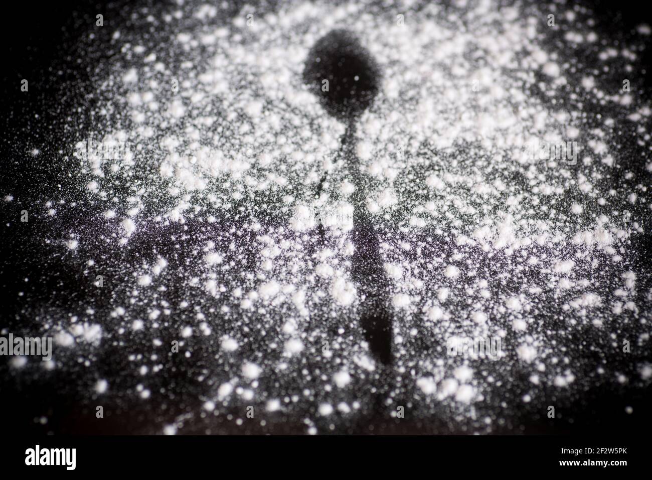 lo zucchero a velo bianco dolce e il cucchiaio si tracciano su sfondo nero Foto Stock