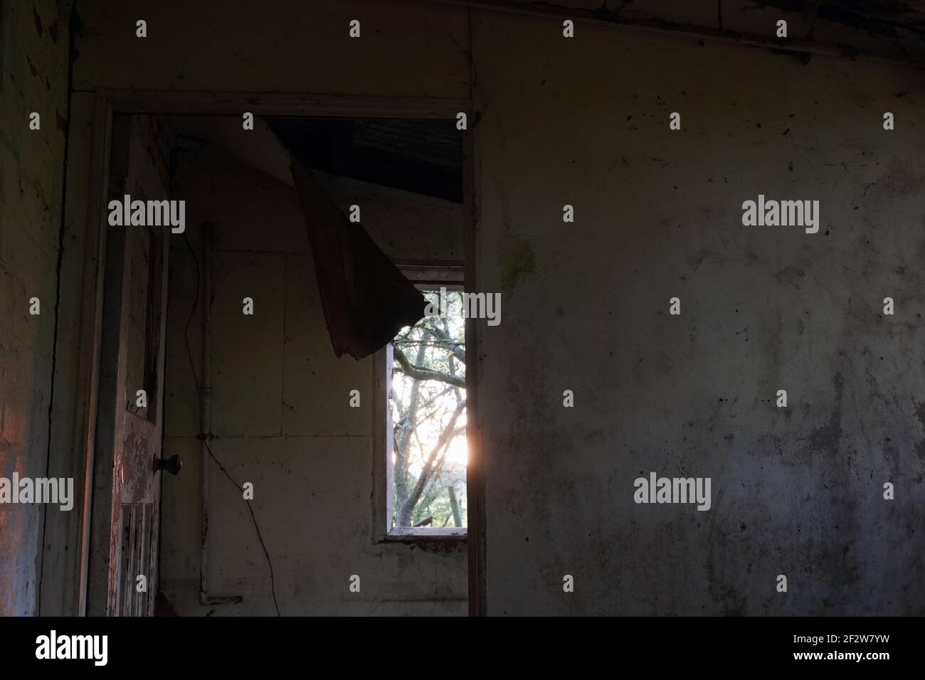 Si affaccia su una finestra al tramonto in una casa infuocata abbandonata. Con pareti in rovina e soffitto rotto. Foto Stock