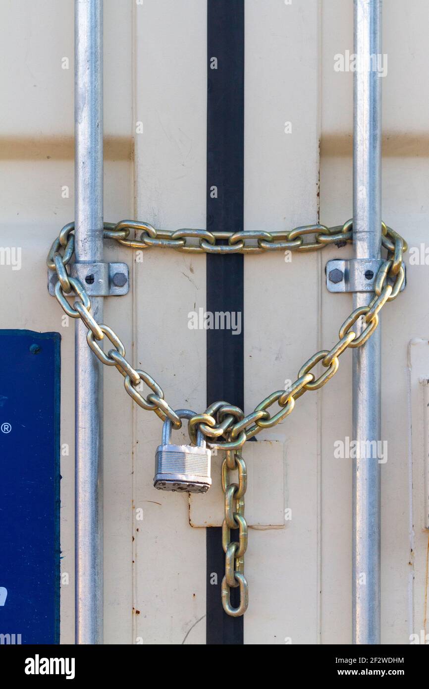 Un lucchetto di dimensioni industriali per impieghi pesanti è stato fissato a catene in acciaio all'ingresso di un contenitore esterno che immagazzina utensili e attrezzature. I versatile Foto Stock