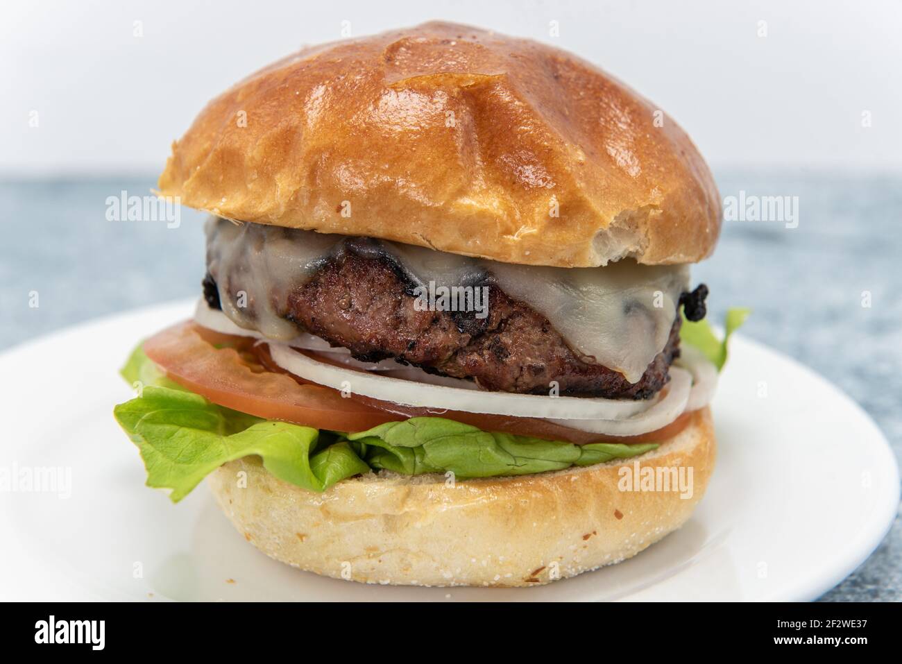 Hamburger accatastato con formaggio fuso seduto su cipolla, pomodori, lattuga e panna per un pasto delizioso. Foto Stock