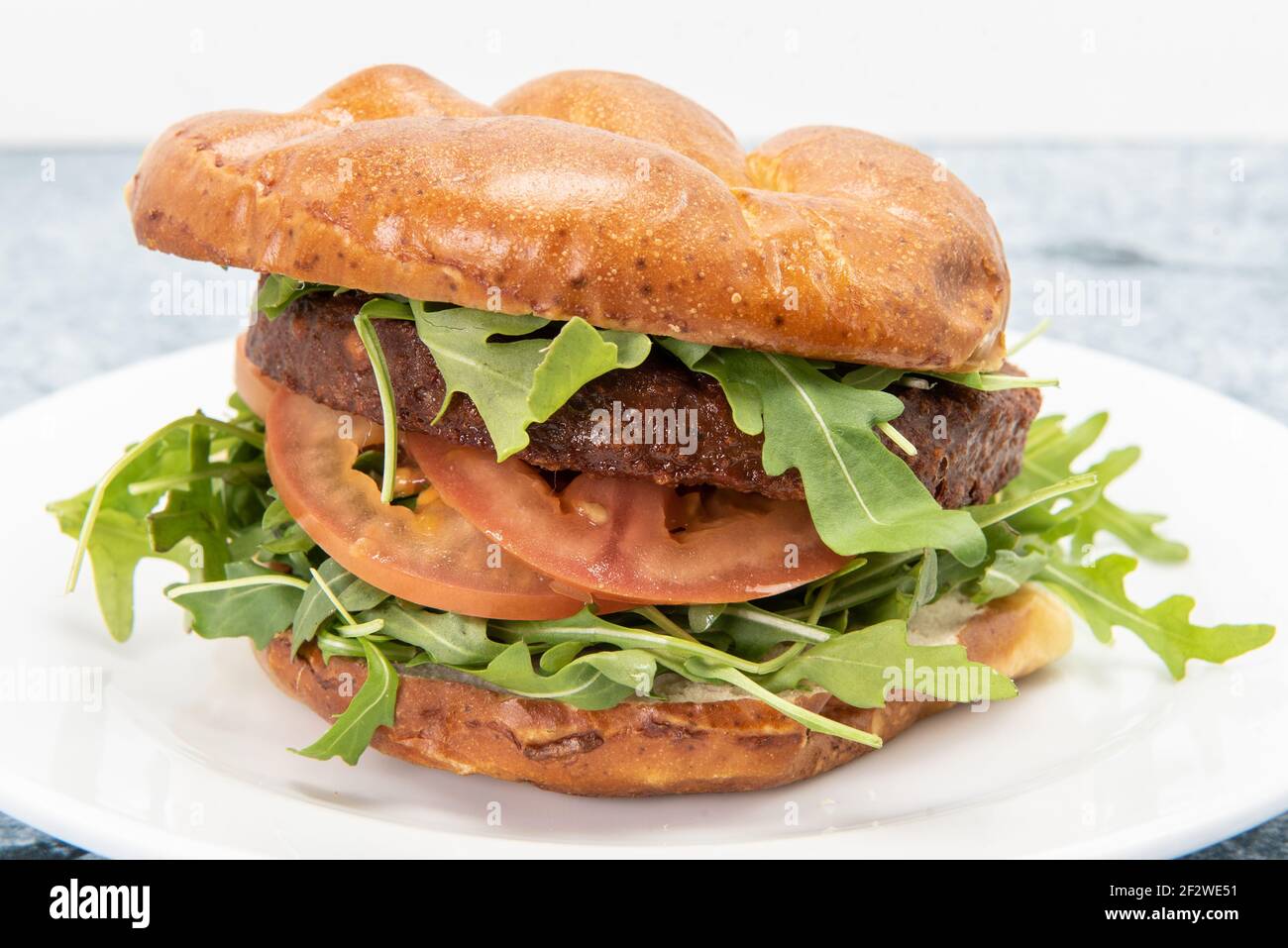 I vegani attenti alla salute possono gustare questo hamburger vegano servito con rucola, pomodori e accatastati all'interno di un panino Foto Stock