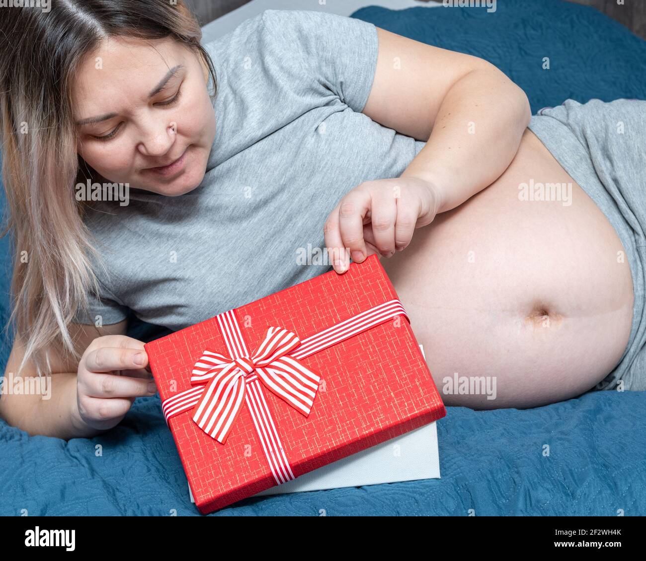 Giovane donna incinta sdraiata sul letto, apre una confezione regalo. Regalo  di compleanno, Festa della mamma, San Valentino, Natale Foto stock - Alamy