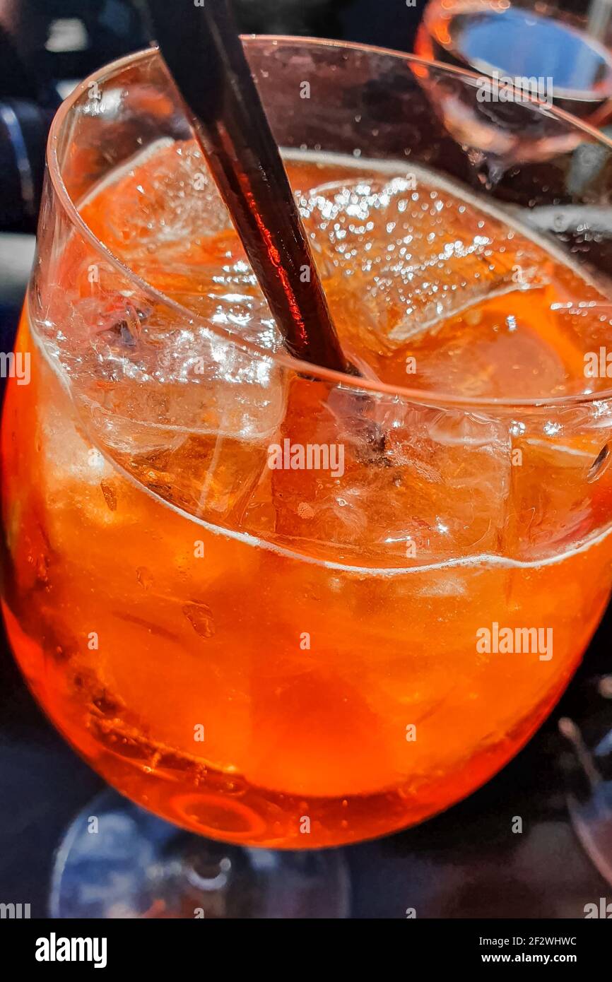 Bicchiere di Aperol Spritz con paglia nera, servito su una terrazza bar che si affaccia sulla città di Manarola, cinque Terre, Italia. Foto Stock