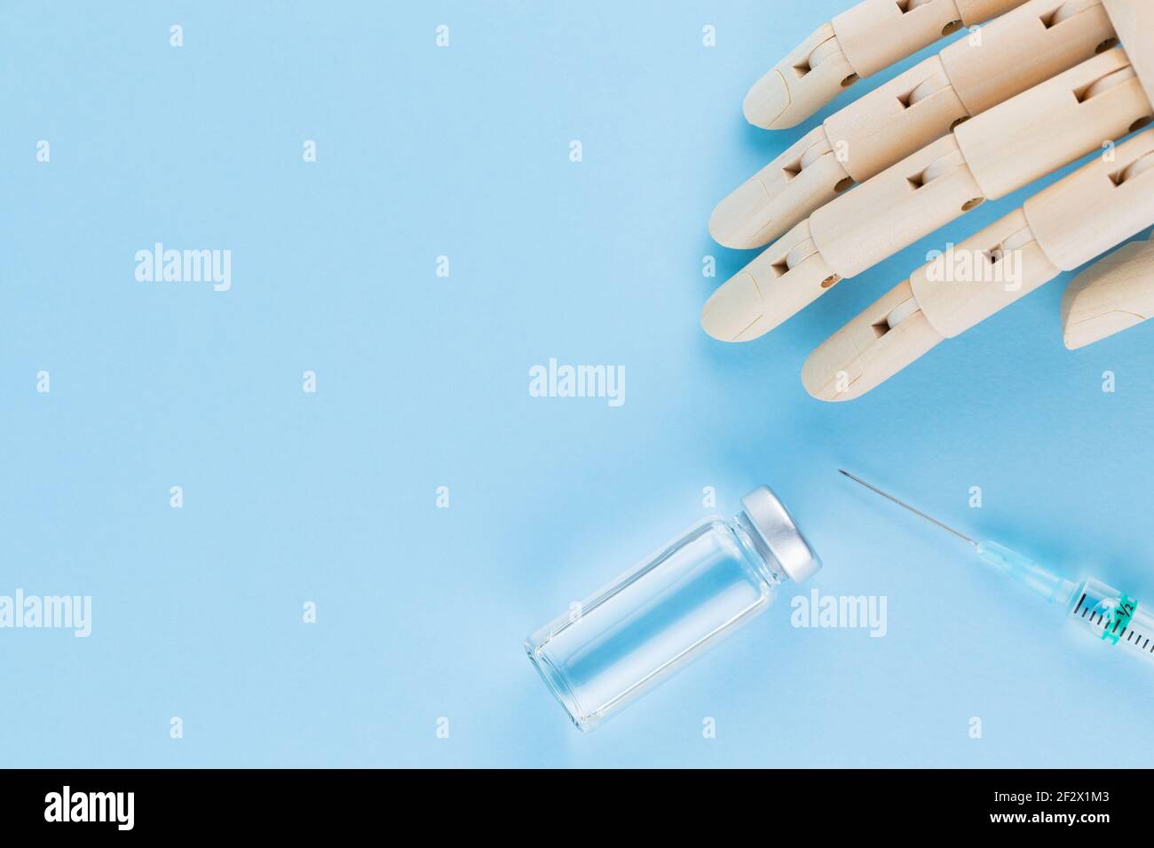 Vaccino, siringa e mano umana di legno. Fiala medica e siringa su sfondo blu. Concetto di assistenza sanitaria e prevenzione delle malattie. Vista dall'alto Foto Stock