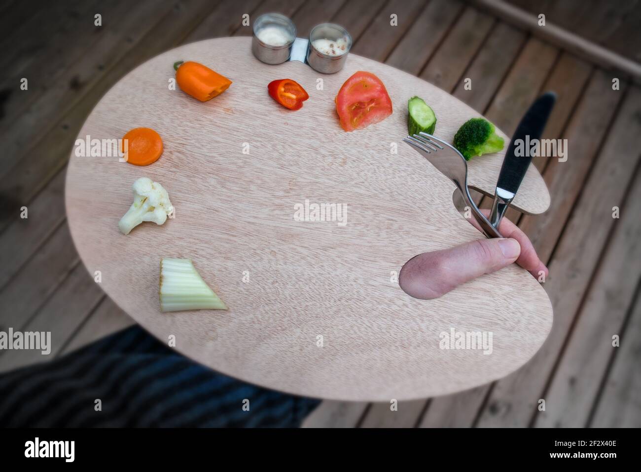 Artista tavolozza di legno su cui sono collocate le verdure. Nelle tazze c'è un bagno di verdure. Un coltello, una forcella e la mano di un maschio. Foto Stock