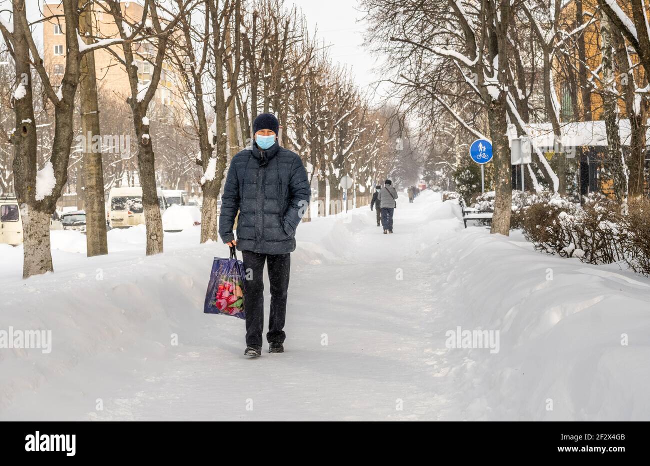 Lutsk, Ucraina - Febbraio 12,2020: Via della città dopo la bizzard. Uomo che indossa la maschera facciale sulle strade pubbliche in mezzo all'epidemia di coronavirus in inverno Foto Stock