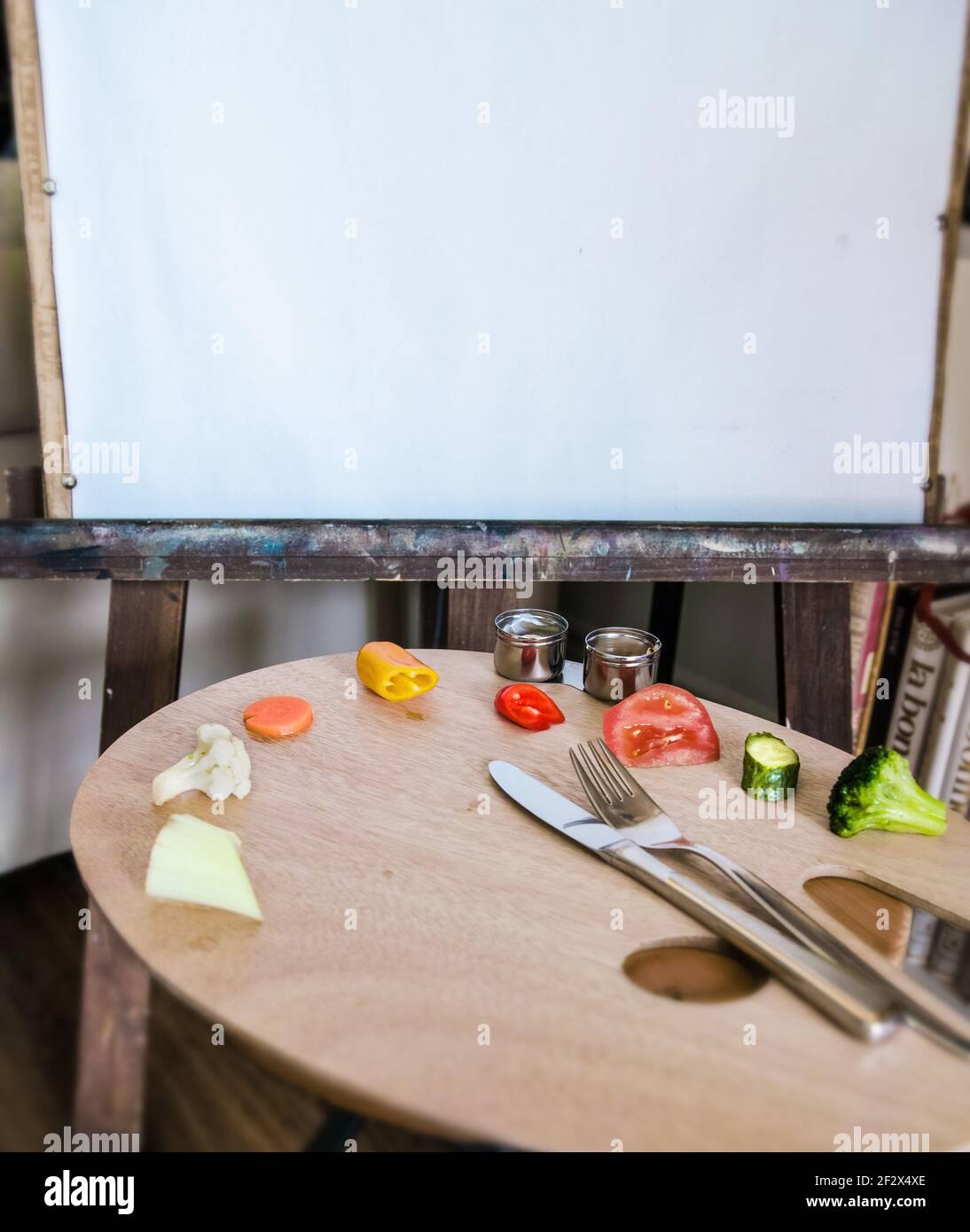 Artista tavolozza di legno su cui sono collocate le verdure. Nelle tazze c'è un bagno di verdure. Un coltello e una forcella. Area di lavoro sullo sfondo per lo spazio di copia. Foto Stock