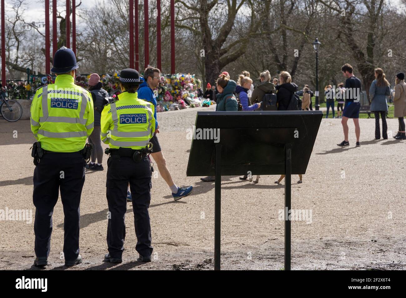 Il poliziotto e la donna osservano le persone che gettano tributi floreali al chiosco comune Clapham in memoria di Sarah Everard, rapito e assassinato , Londra, Inghilterra Foto Stock