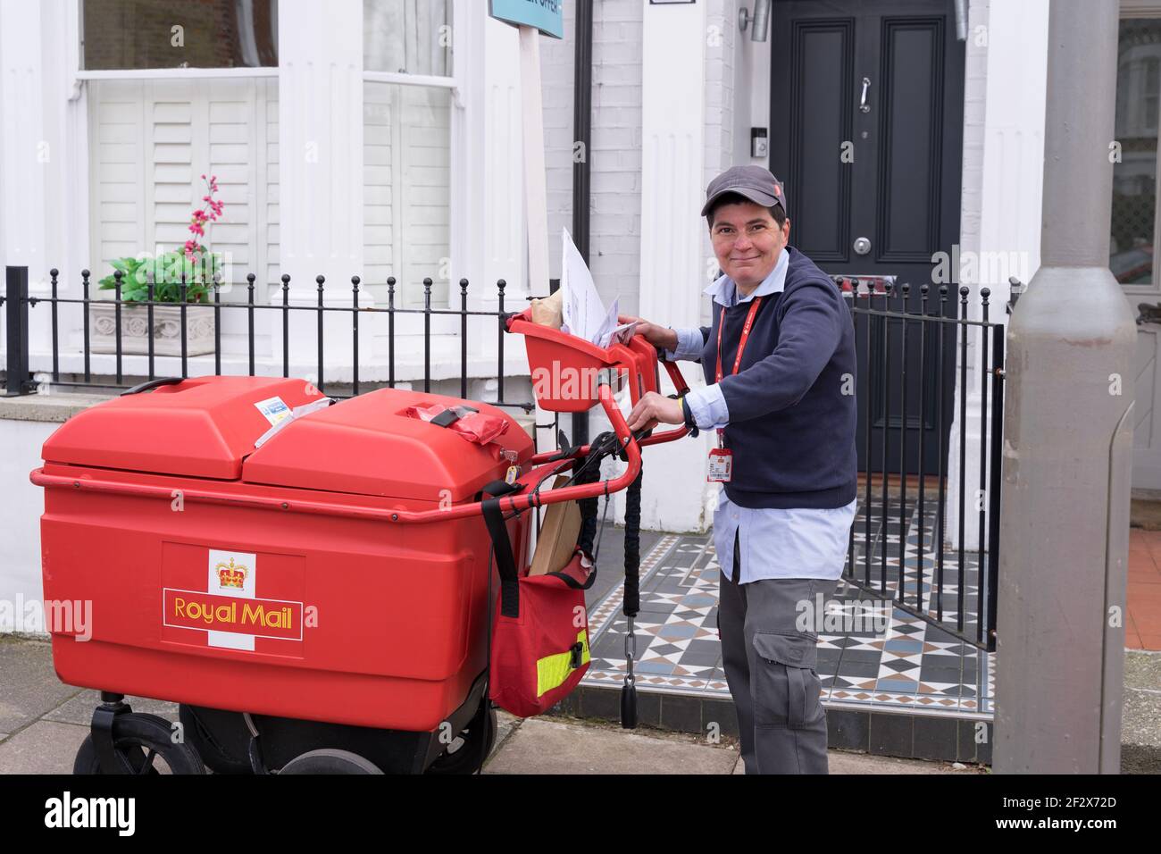 la signora postale reale sorride in piedi accanto al suo carrello postale, carrello che consegna posti e pacchi ai residenti in clapham comune , londra sud, Regno Unito Foto Stock
