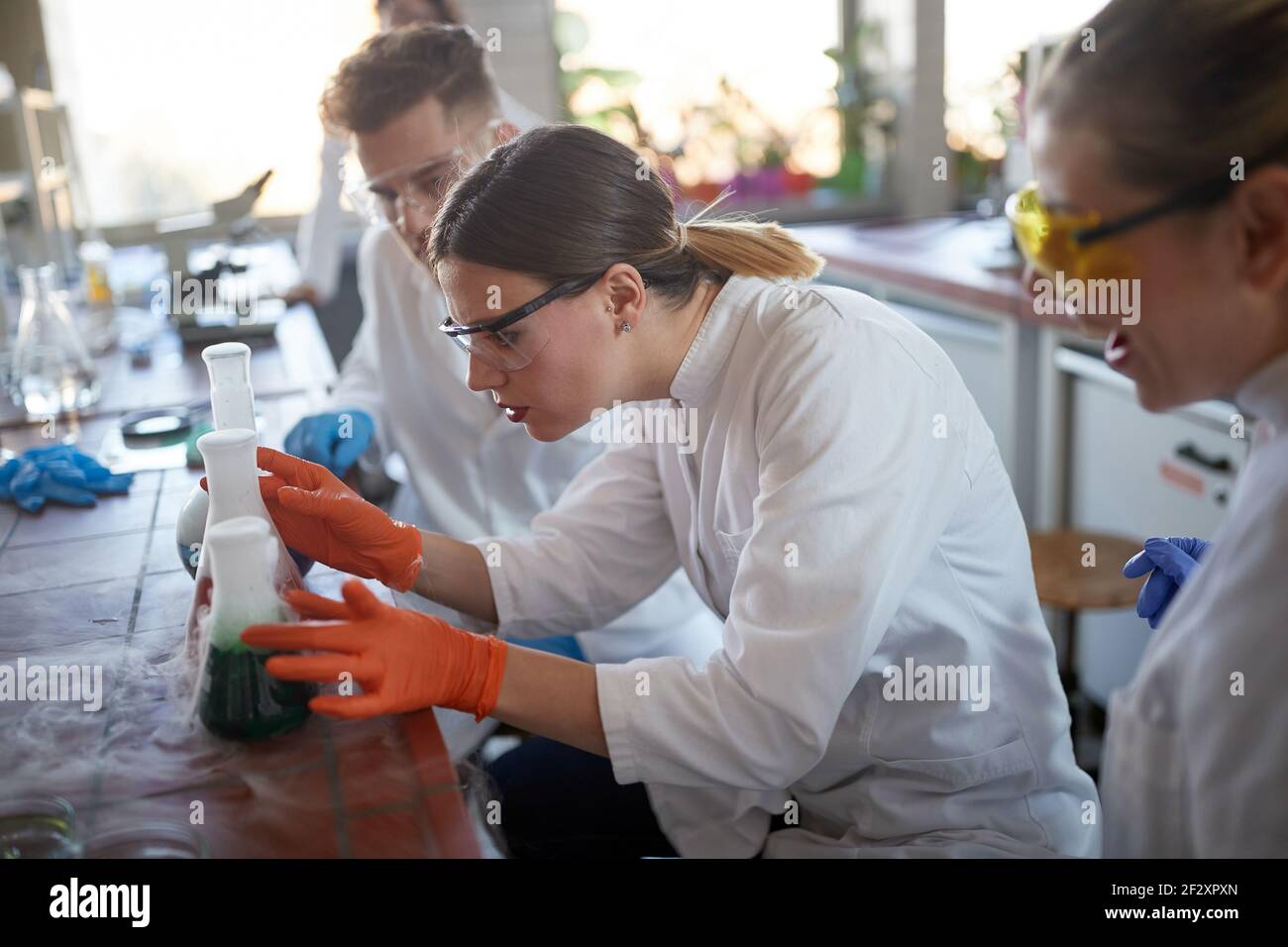 Tre tecnici laboranti che esaminano le reazioni chimiche in laboratorio Foto Stock