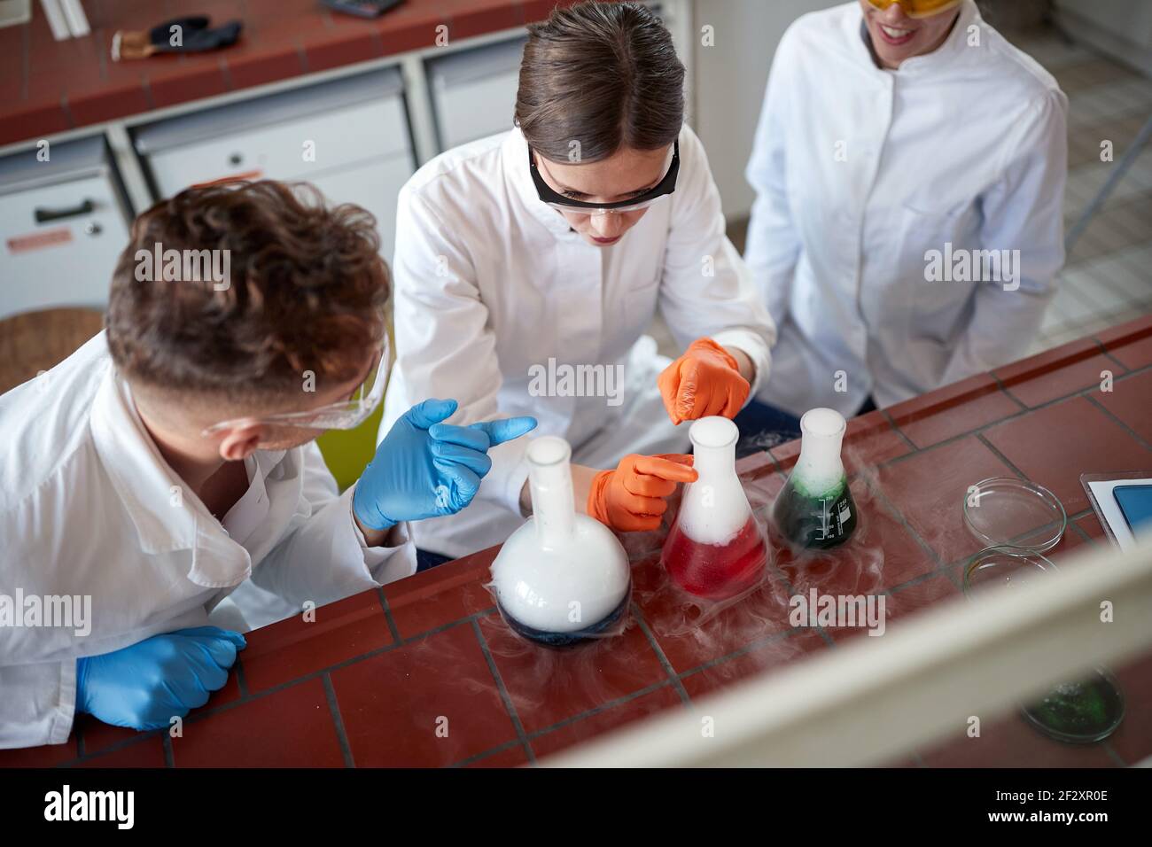 Tre giovani tecnici laboranti che esaminano le reazioni chimiche in laboratorio Foto Stock
