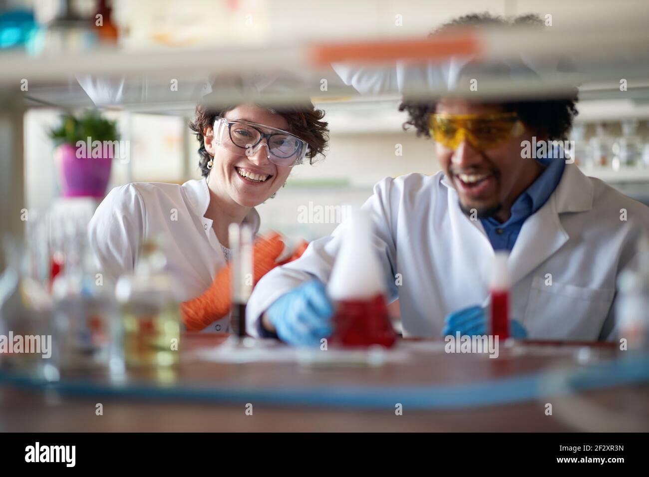 I giovani colleghi in un abbigliamento protettivo possono lavorare con prodotti chimici colorati in un'atmosfera rilassata nel laboratorio universitario. Scienza, chimica, laboratorio Foto Stock