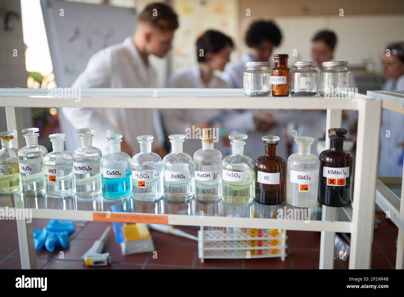 Diversi prodotti chimici sullo scaffale e giovani studenti in un ambiente di laboratorio universitario sterile. Scienza, chimica, laboratorio, persone Foto Stock
