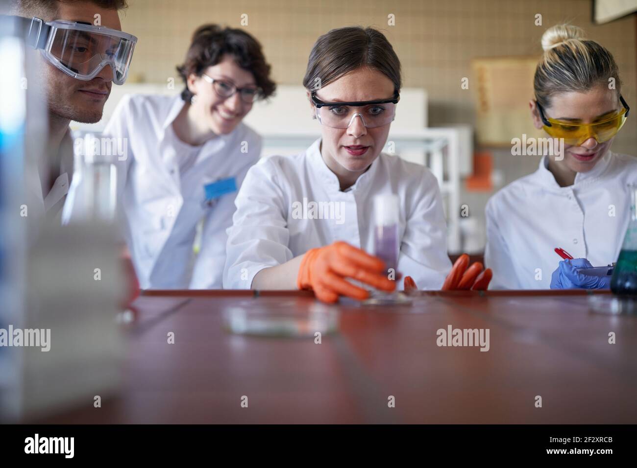 Quattro tecnici laboranti che esaminano le reazioni chimiche in laboratorio Foto Stock