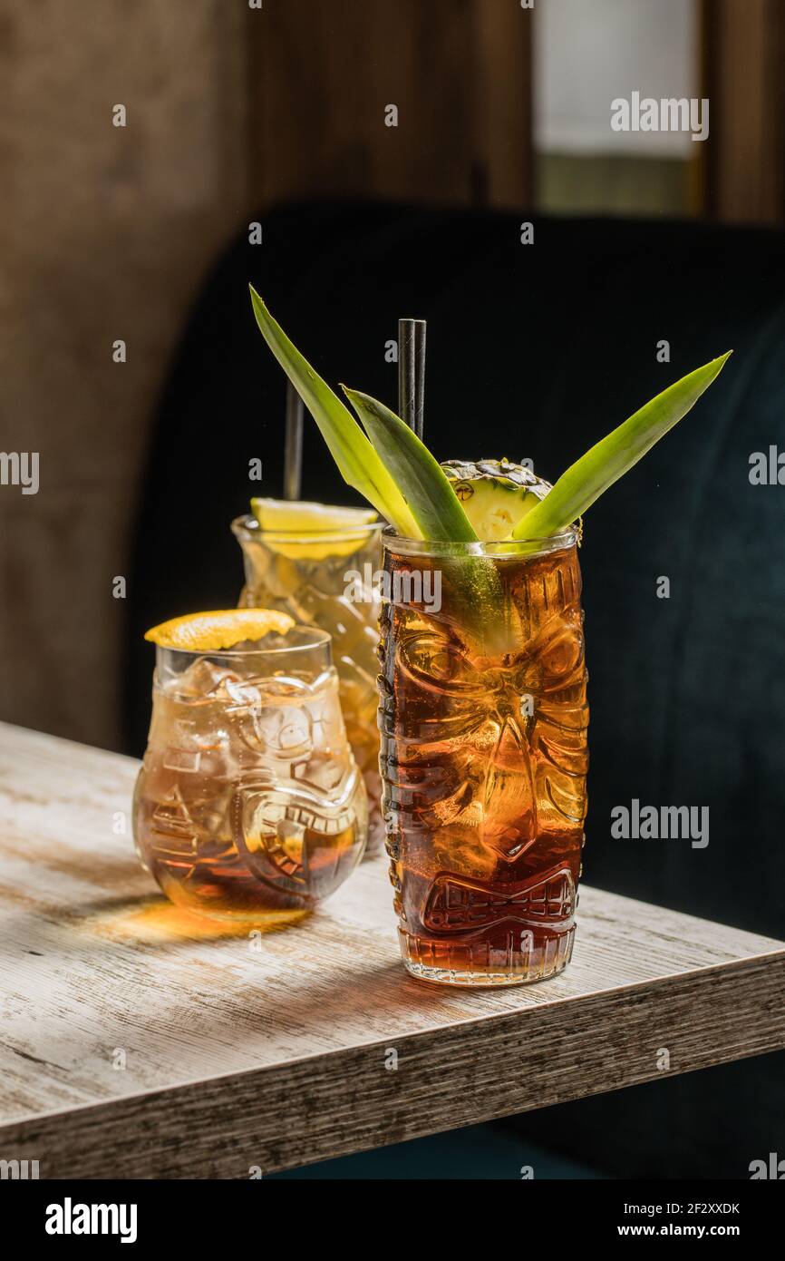 Bicchieri tiki tazza ripieni di bevande alcoliche con decorazioni in paglia  con frutta posta sul bordo del divano di legno del tavolo Foto stock - Alamy