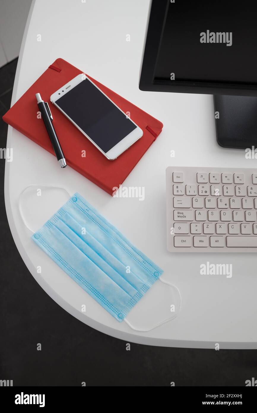 Da sopra computer e smartphone moderni con notebook posizionato sopra tavolo bianco con maschera medica in ufficio leggero Foto Stock