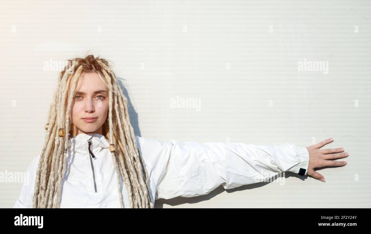 Giovane donna moderna alla moda con capelli biondi dreadlock puntando con la sua mano sul muro Foto Stock